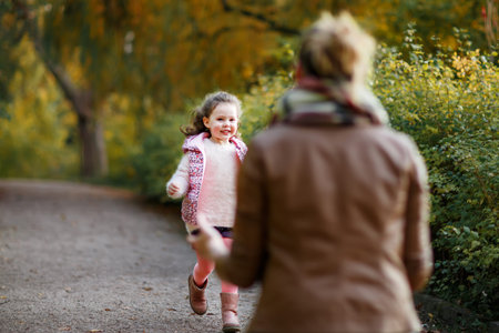 Mother and daughter walking in autumn park together. Happy family enjoying fall season outdoors....