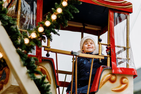 Happy cute preschool girl riding on ferris wheel carousel horse at Christmas funfair or market, outdoors. Little toddler child having fun on traditional family xmas market in Germany.の写真素材