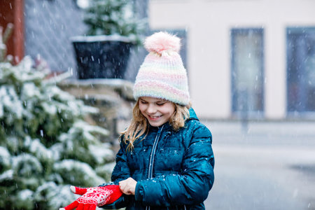 Funny portrait of little school girl in winter clothes. Happy positive child outdoors. Winter day, snow falling. Cold weather and snowingの写真素材