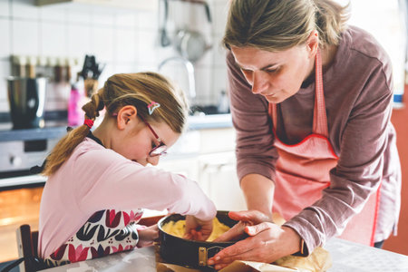 Little cute girl helps her mother bake a cake in the kitchen. Child and woman mixing ingredients with joy, learning to cook in a warm, homey atmosphere.の写真素材