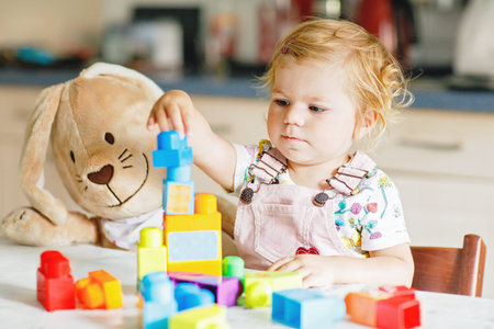 Adorable toddler girl with favorite plush bunny playing with educational toys in nursery. Happy...