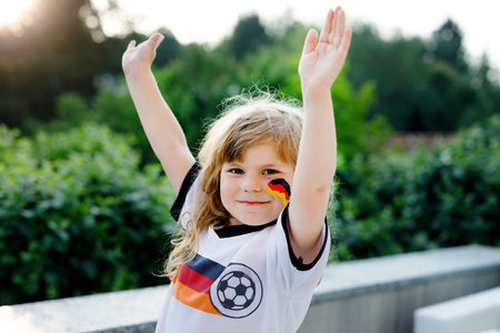 Little blond preschool girl watching soccer football cup game on public viewing. Happy joyful...