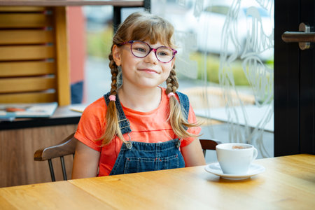 Adorable little girl with glasses drinking hot chocolate indoors. Happy child enjoying warm drink. Real life, real people moment of childhood comfortの写真素材
