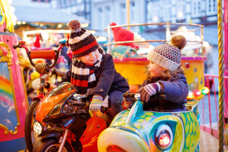 Adorable little boy and girl, siblings on a carousel at Christmas funfair or market, outdoors. Happy children, friends having fun. Selective focus on one child. Holiday, children, lifestyle concept.の写真素材