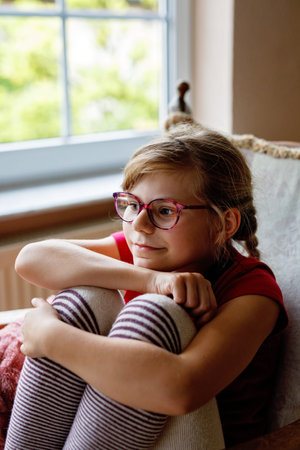 Cozy portrait of little school girl with eyeglasses at home.