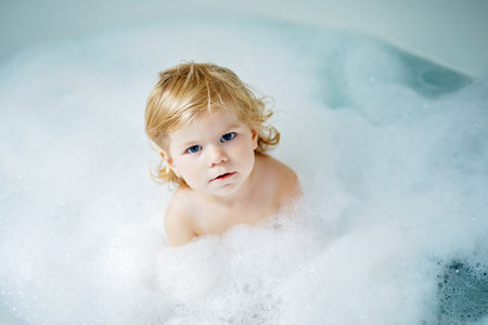 Adorable cute little toddler girl taking bath in bathtub. Happy healthy baby child playing with rubber gum toys and having fun. Washing, cleaning, hygiene for childrenの写真素材