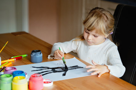 Little preschool girl painting with fingers tree on paper at home or at kindergarten daycare. Child doing creative art activity indoors. Real life, real peopleの写真素材