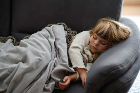 Little girl sleeping on sofa under blanket at home. Child resting peacefully indoors. Real life,...