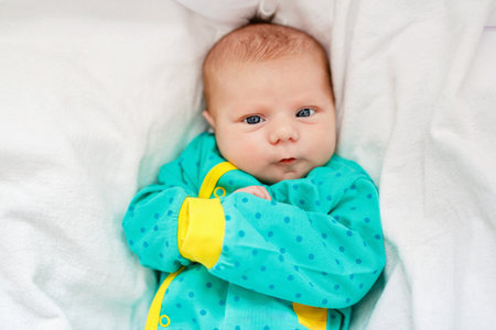 Cute adorable newborn baby in white bed and wrapped in blanket. New born child, little girl looking surprised at the camera. Family, new life, childhood, beginning concept.の写真素材