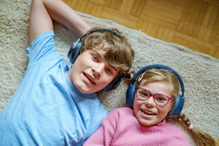 Two children, a teenage boy and a little girl, listening to music together with headphones. Smiling happy siblings enjoying sound and spending fun leisure time indoors.の写真素材