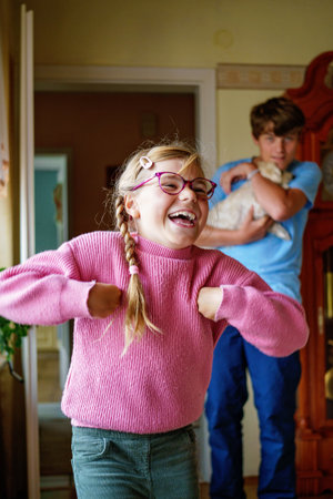 Two children, a teenage boy and a little girl, laughing and having fun indoors. Smiling happy siblings enjoying each other's company and spending fun leisure time at home.の写真素材