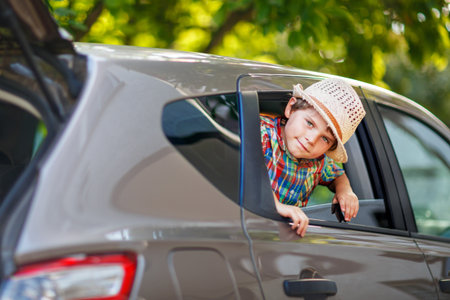 Little boy sitting in car and waving while family goes on summer road trip. Happy child enjoying travel, real life, real people.の写真素材