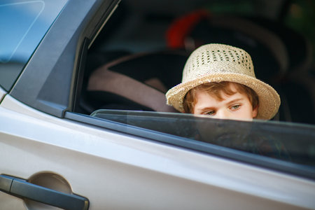 Sad little kid boy sitting in car during traffic jam on the way to summer vacation with his parents....