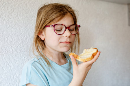 Little school girl eating bread with butter for breakfast. Happy cute child with eyeglasses having healthy snack.の写真素材