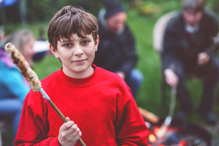 Teenager boy roasting bread stick on fire in teen camp in summer. Happy child spending vacations in sports camp.の写真素材
