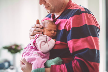 Happy father holding his newborn baby girl in arms. Cute little infant sleeping peacefully on dad chest at home. Family love, bonding and parenthood concept.の写真素材