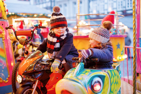 Adorable little boy and girl, siblings on a carousel at Christmas funfair or market, outdoors. Happy children, friends having fun. Selective focus on one child. Holiday, children, lifestyle concept.の写真素材