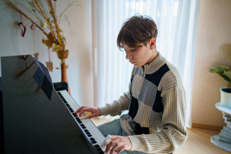 Teen boy playing piano at home. Teenager having fun with play music instrumentの写真素材