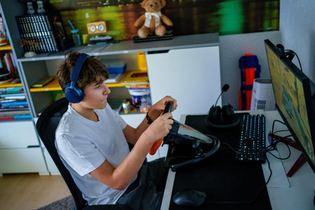 Teen boy playing racing video game with steering wheel at home