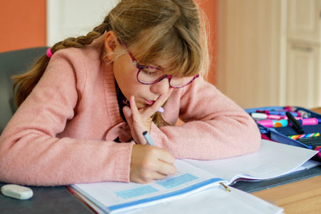 Cute elementary school girl writing in her workbook and doing school homework. Focused child...