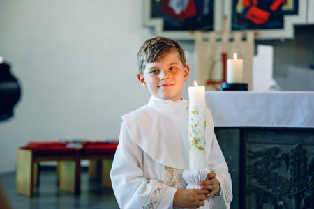 Little kid boy receiving his first holy communion. Happy child holding Christening candle. Tradition...