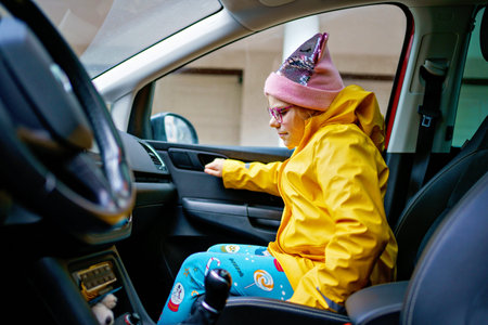 Little schoolgirl in yellow raincoat with backpack on a residential street, real life morning...