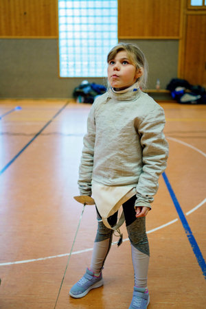 Young girl practices fencing indoors, focused and confident during a training session in a sports...