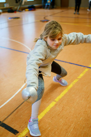 Young girl practices fencing indoors, focused and confident during a training session in a sports...