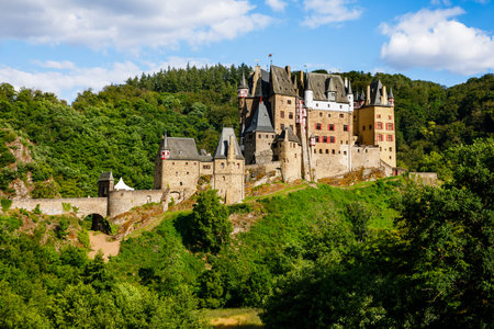 Majestic medieval Eltz Castle surrounded by lush green forest in summer sunlight. Historic...