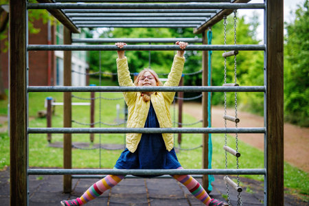 Little girl doing gymnastics on a climbing frame, horizontal bar on school yard. Child enjoying...