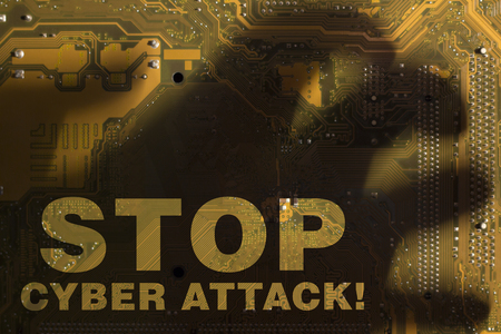 The inscription "Stop cyber attack" through the shadow of the hand on the yellow motherboard.の写真素材