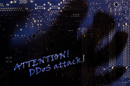 The inscription Attention DDoS attack through the shadow of the hand on the blue motherboard.
