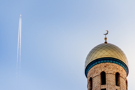 The Muslim minaret of the mosque against the blue sky with the plane flying far.の写真素材