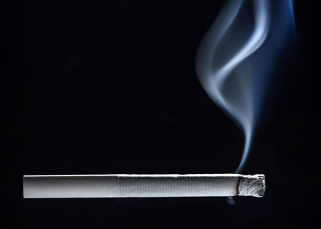 A white cigarette close-up begins to smolder tobacco and a trickle of smoke rises up.