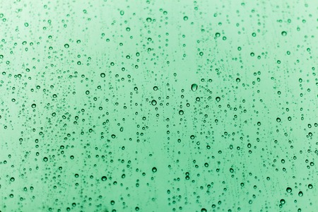 Drops of water of different sizes on a green transparent glass background.の写真素材