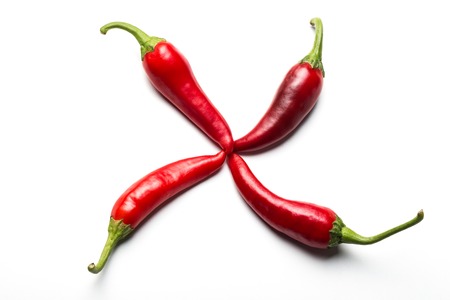Four red chili peppers in the form of a cross on a white background.の写真素材