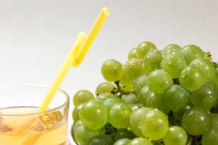 A beautiful ripe grapes with water drops and an edge of a glass with juice and a yellow tube for a cocktail.の写真素材