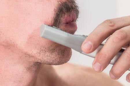 Unshaven man cuts his mustache with a manual trimmer without wires. Side view. Close-up.の写真素材