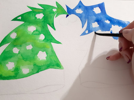 The girl's hand draws a blue and green fir-tree with a watercolor paint.の写真素材