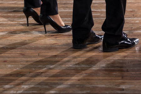 Male and female legs in black shoes and trousers on an old wooden parquet floor. Close up.の写真素材