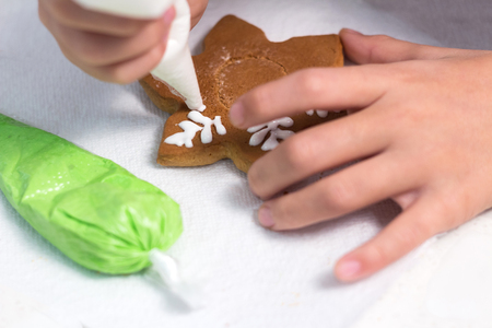 Cookies in the form of a snowflake. Close-up. The child decorates handmade Christmas gingerbread with glaze.の写真素材