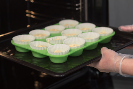 Blurred background. The chef's hands in transparent gloves insert green molds with a cupcakes dough...