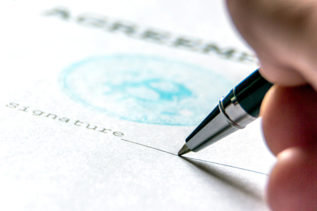 A ballpoint pen in the person's hand on a piece of paper with a bitcoin stamp puts a signature. Macro. The concept of the contract of purchase for bit-coin.の写真素材