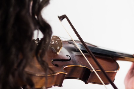 Girl playing the violin. The bow touches the strings. Close-up. View from the shoulder side through the hair. Musical theme. White background.の写真素材