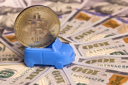 Concept of high cost, money exchange, car loan or purchase of vehicles for crypto currency. A miniature retro cabriolet carries gold bitcoin against the background of hundred-dollar bills spread out in a circle. Close-up.の写真素材