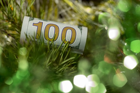 A hundred-dollar bill collapsed with a straw is on the branches of the New Year's spruce. Concept How much does Christmas cost or a gift for a New Year's holiday. Copy space.の写真素材