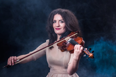 Beautiful brunette girl in a light beige dress playing the violin. Concept for music news. Smoky...