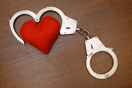 Red soft heart and real steel police handcuffs on a brown background. The concept of love and the law.の写真素材