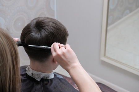 Female hands with scissors cut off the ends of the hair on the guy's head. Close-up of haircuts in a hairdresser.の写真素材