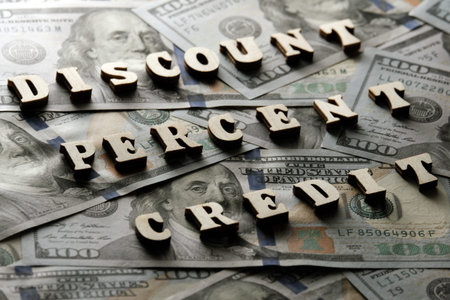 DISCOUNT, PERCENT, CREDIT is laid out of wooden letters on the background of hundred-dollar bills....